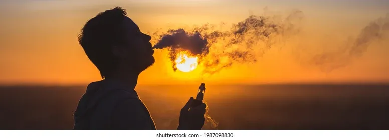A person sitting on a balcony watching the sunset, thoughtfully browsing an online vape shop on a tablet or laptop, representing the digital planning experience.