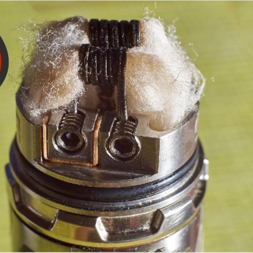 A magnified close-up of a heavily gunked or caramelized vape coil, showing dark, crusty residue built up on the heating wire and cotton wick, indicating flavor loss.