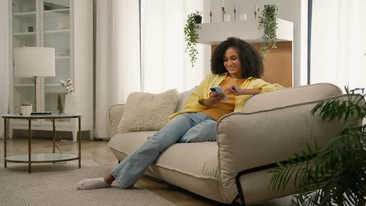 A person on a cozy couch, wrapped in a blanket, scrolling through a phone on a rainy evening, online shopping for home decor.