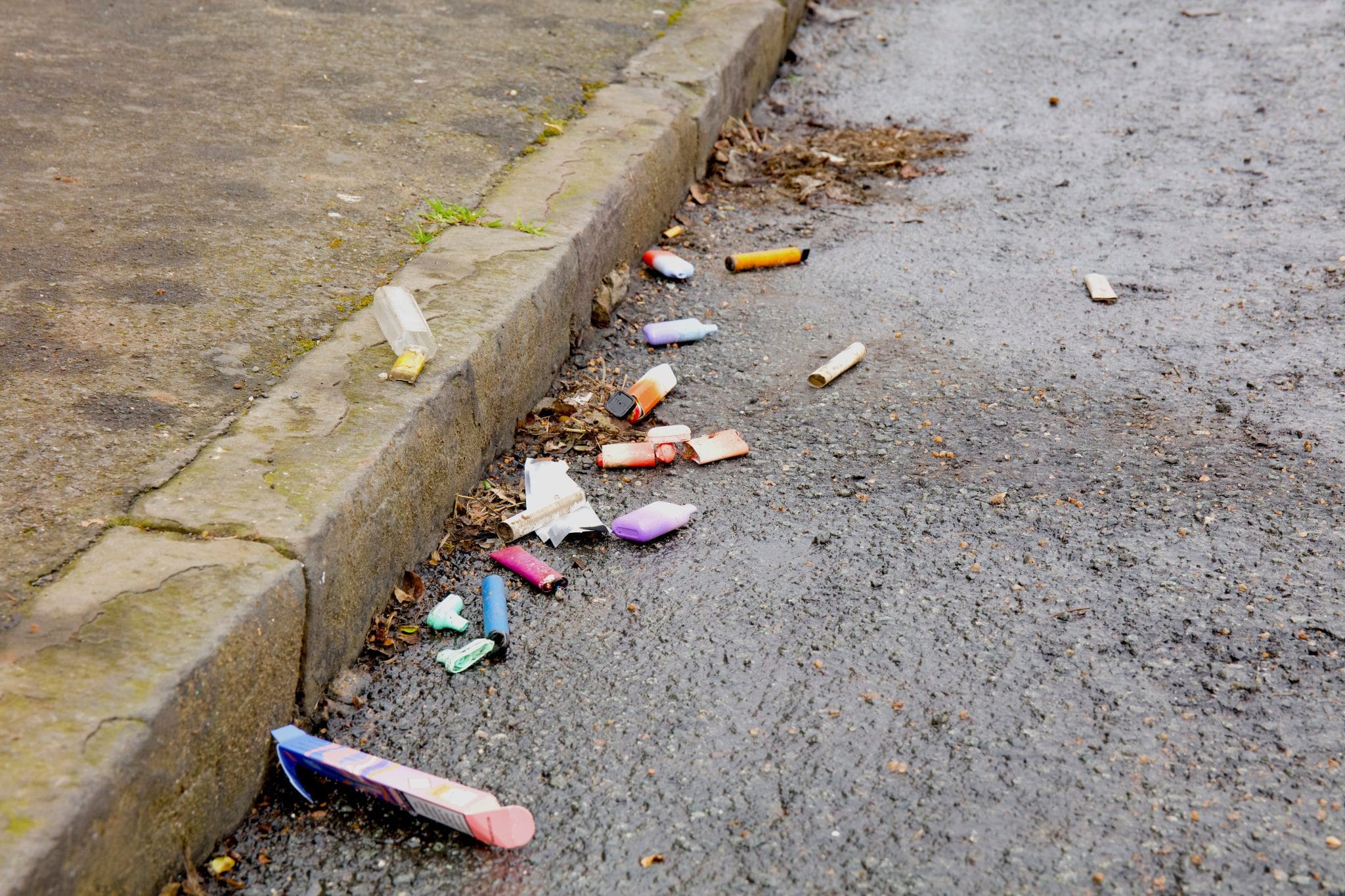 Discarded disposable vapes scattered on a beach, park, or roadside, symbolizing the environmental impact and pollution from electronic waste.