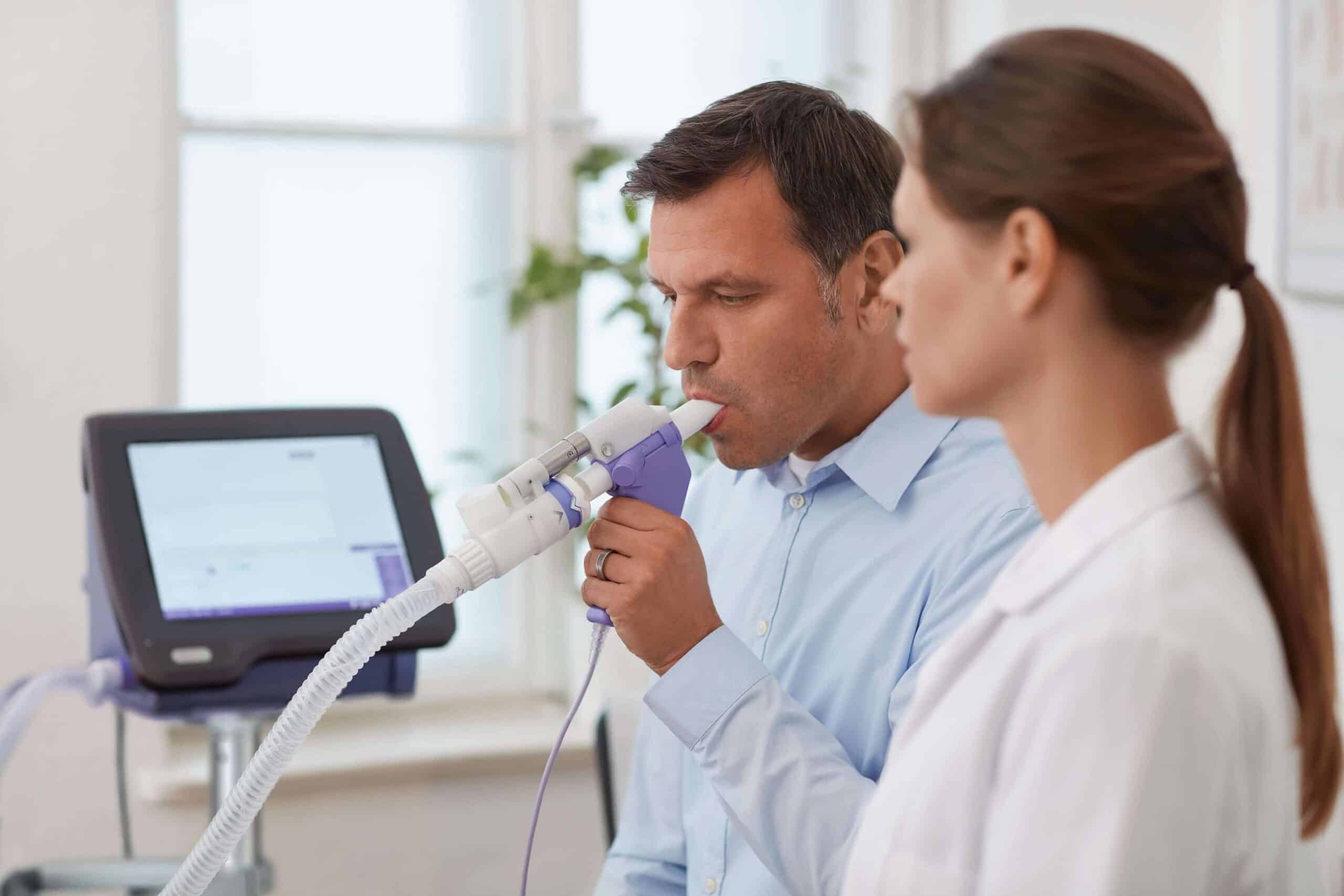 A doctor (GP) performing a spirometry lung function test on a patient in a clinic.