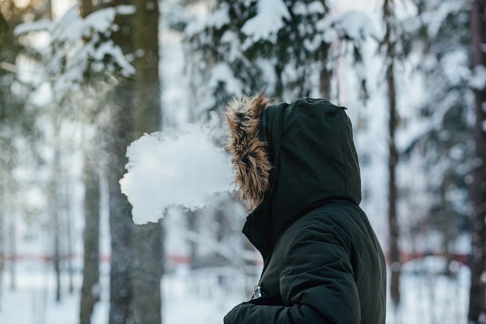 A persons hand placing a disposable vape into an interior jacket pocket, suggesting the use of body warmth to protect the device from cold.